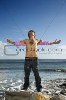 Young Man Standing on Ocean Rock with Arms Outstretched