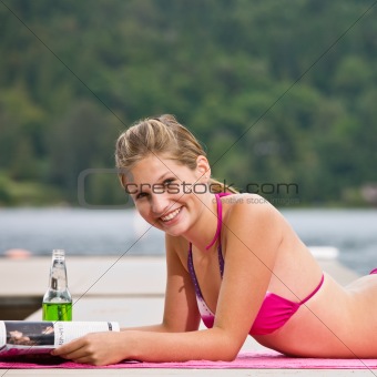 Woman laying on pier reading magazine