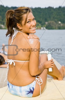 Woman sitting on pier applying sunscreen lotion