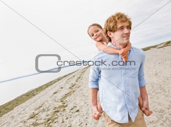 Father giving daughter piggy back ride at beach
