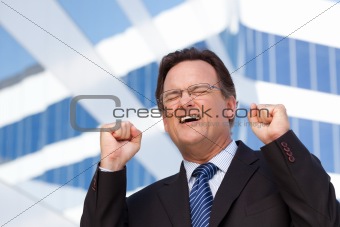 Excited Businessman in Suit and Tie Clinches His Fists in Joy Outside of Corporate Building.