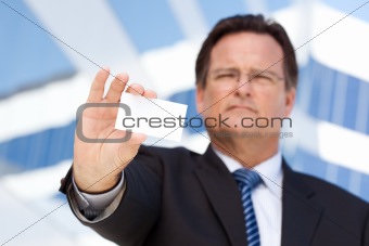 Handsome Businessman in Suit and Tie Holds Out Blank Business Card in Front of Corporate Building.