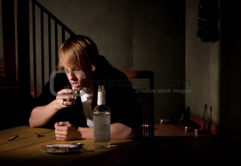Depressed young man with bottle of clear alcohol