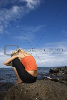 Upset woman sitting on rocky shore.