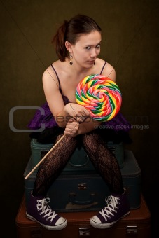 Pretty girl in funky purple outfit on green background with big lollipop