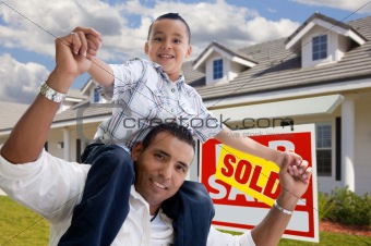 Excited Hispanic Father and Son with Sold For Sale Real Estate Sign in Front of House.