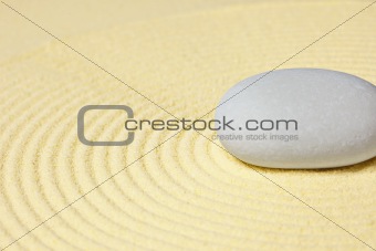 Round stone lying on sand with circular pattern