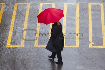 woman with red umbrella walking on pedestrian crossing in rain