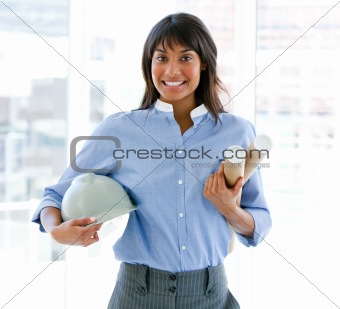 Smiling female architect holding a hardhat and blueprints standi