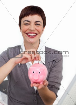 Smiling businesswoman saving money in a piggybank in the office
