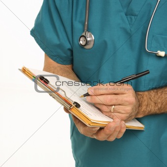 Doctor in scrubs making notes on a patient's chart.