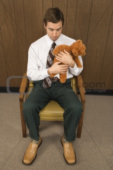 Man sitting in chair holding a stuffed animal looking sad.