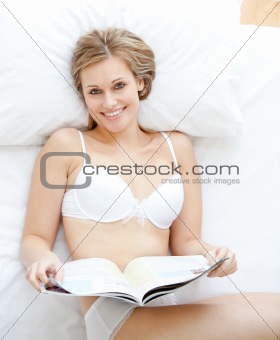 Happy woman reading a magazine lying on a bed 