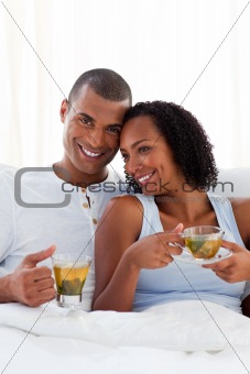 Affectionate couple drinking a cup of tea on their bed