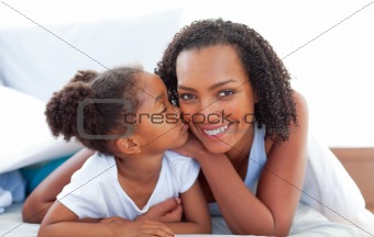 Loving little girl woman kissing her mother lying down on bed