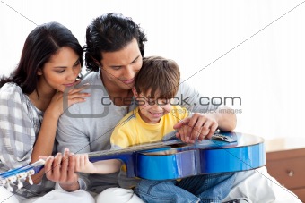 Happy little boy playing guitar with his parents