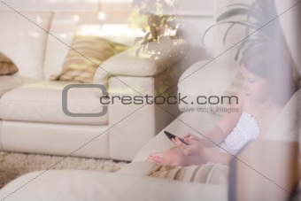 Young girl sitting in a sofa and using phone behind the glass window 