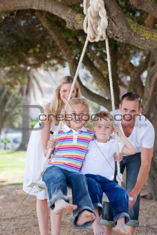 Happy parents pushing their children on a swing 