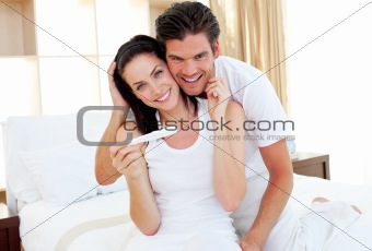 Blissful couple finding out results of a pregnancy test sitting on bed