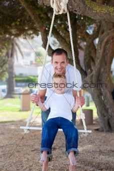 Happy father pushing his son on a swing 