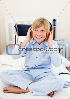 Smiling boy listening music sitting on bed