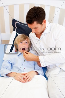 Worried father checking his son's temperature in the bedroom