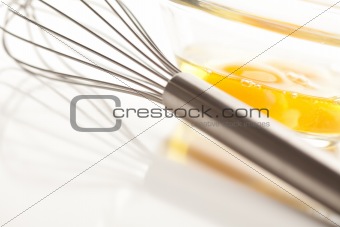 Hand Mixer with Eggs in a Glass Bowl on a Reflective White Background.