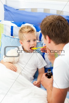 Affectionate father giving cough syrup to his sick son