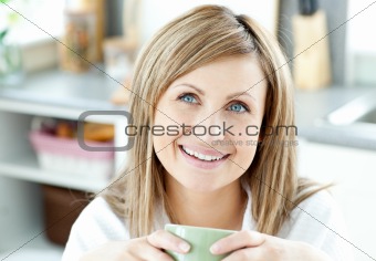 Happy woman holding a cup of coffee in the kitchen 