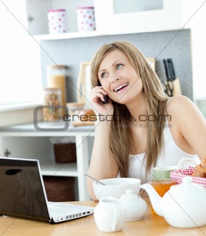Delighted woman using a phone and laptop in the kitchen