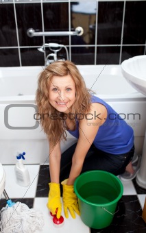 Positive young woman cleaning bathroom's floor 