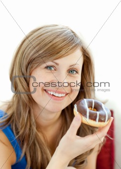 Delighted woman is eating a donut on a sofa 