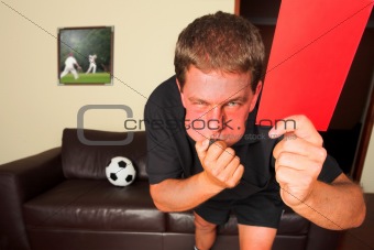 Referee in sitting room blowing whistle with red card 
