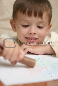 A smiling boy draws behind a table