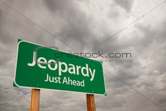 Jeopardy Just Ahead Green Road Sign with Dramatic Storm Clouds and Sky.