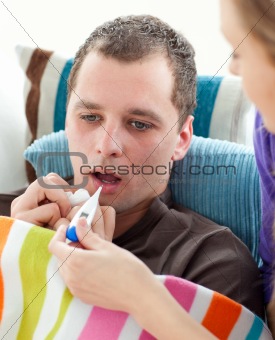 Attentive woman taking her sick husband's temperature on a sofa