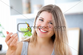 Cute woman eating a salad in the kitchen at home
