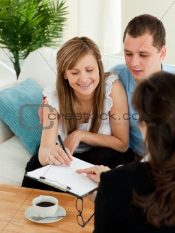 Bright young couple signing a contract sitting in their living r