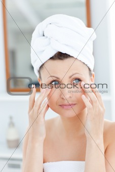 Attractive young woman with a towel putting cream on her face