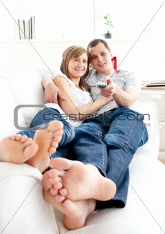 Young happy couple watching tv lying on the sofa 