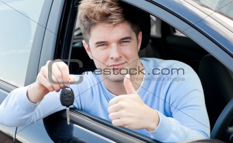 Positive young man holding a key sitting in a car 