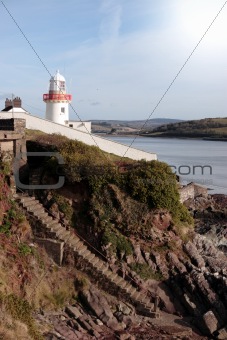 lighthouse with steps down to rocky beach during a sunny day