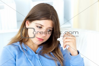 Sad young woman holding tissues sitting in the living-room 