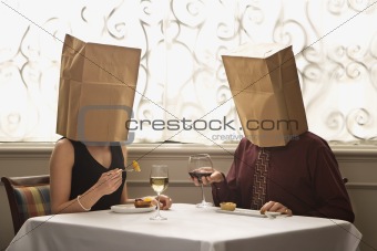 Couple dining wearing bags on heads.