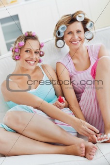 Cheerful female friends doing pedicure and wearing hair rollers 