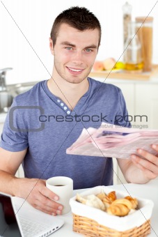 Positive young man holding a cup and a newspaper smiling at the 