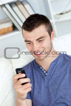 Charming young man sending a text and smiling in the living-room