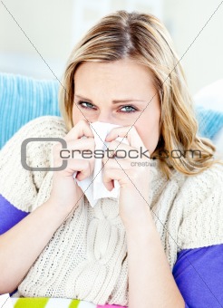 Ill woman using a tissue sitting on a sofa