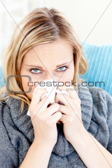 Sick woman using a tissue sitting on a sofa