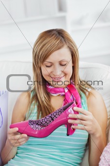 Charming caucasian woman holding a pink shoe on a sofa